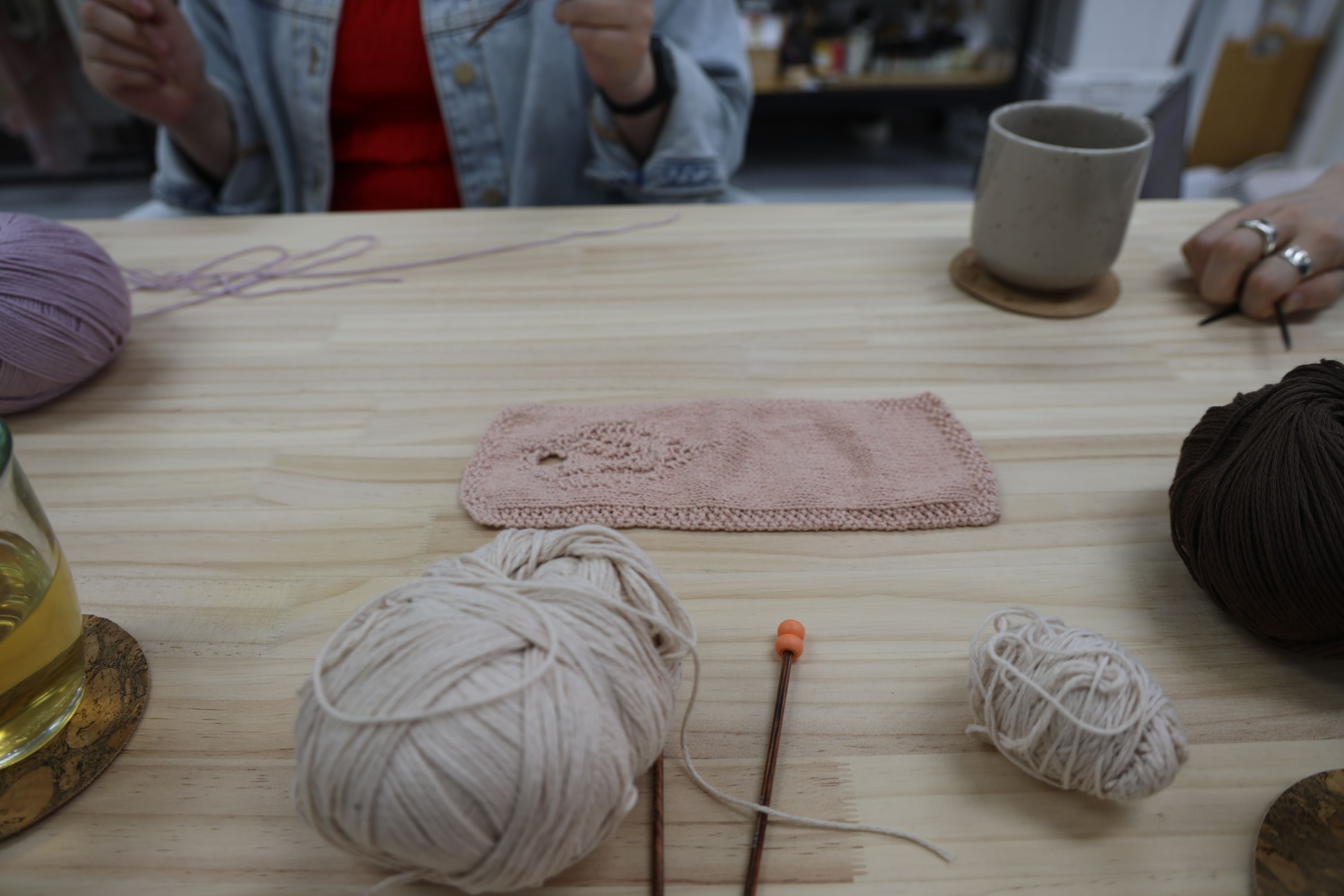Completed knitted piece in pink alongside yarn and needles