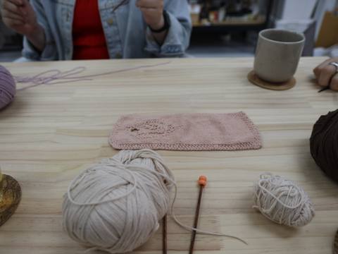 Completed knitted piece in pink alongside yarn and needles