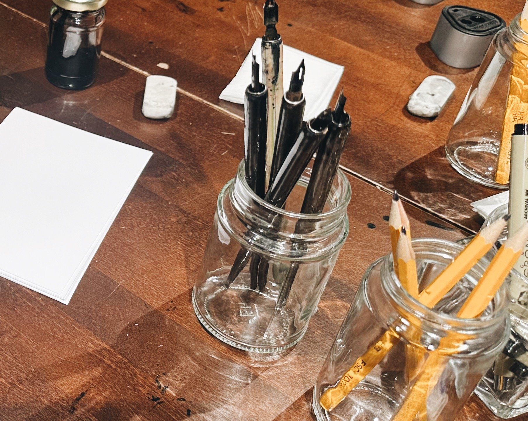 Dip pens, ink, and pencils laid out on the studio table