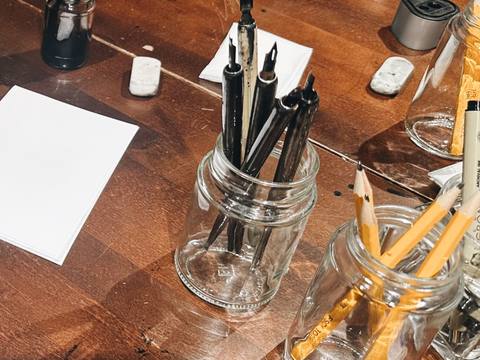 Dip pens, ink, and pencils laid out on the studio table
