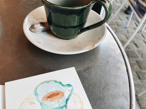 Watercolor drawing of a green coffee cup next to the real cup