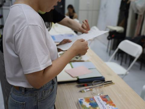 A participant reading a printed handout at the table — Material Lab × AI Archiving, July 15, 2026