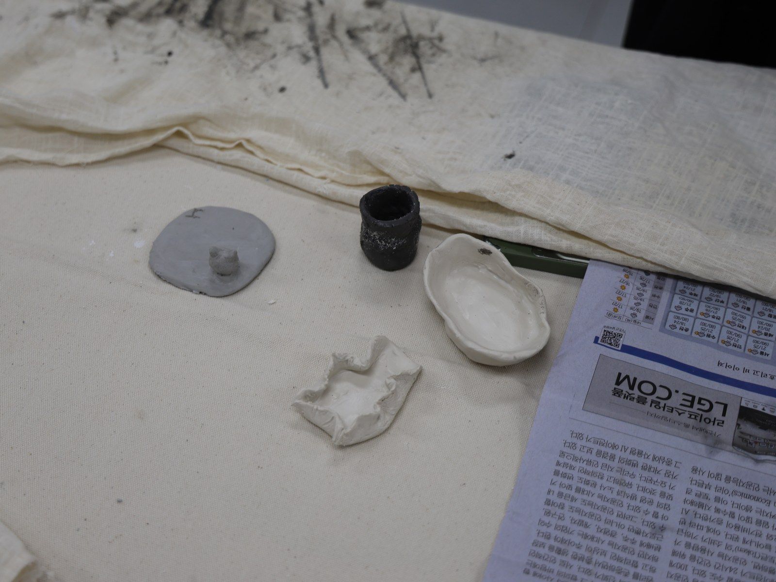 Finished ceramic and clay pieces beside a newspaper clipping — Material Lab × AI Archiving, July 15, 2026