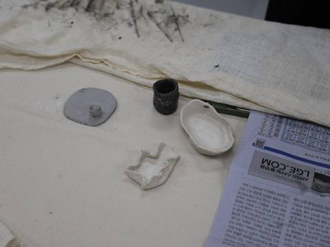 Finished ceramic and clay pieces beside a newspaper clipping — Material Lab × AI Archiving, July 15, 2026