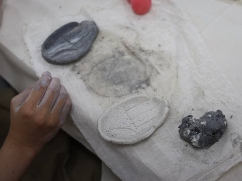 A hand beside grey molded clay pieces on cloth — Material Lab × AI Archiving, July 15, 2026