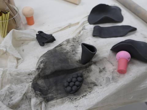 A hand pointing at a small stamped clay tile beside a pastel drawing — Material Lab × AI Archiving, July 15, 2026